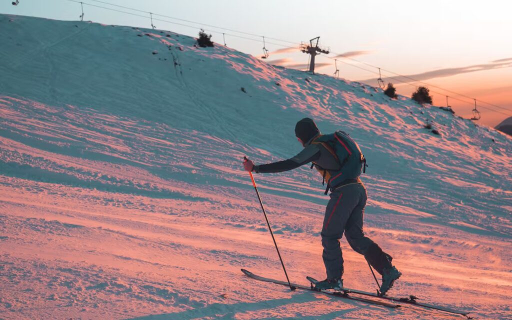A skier ascends a snowy slope with skis during a vibrant sunrise