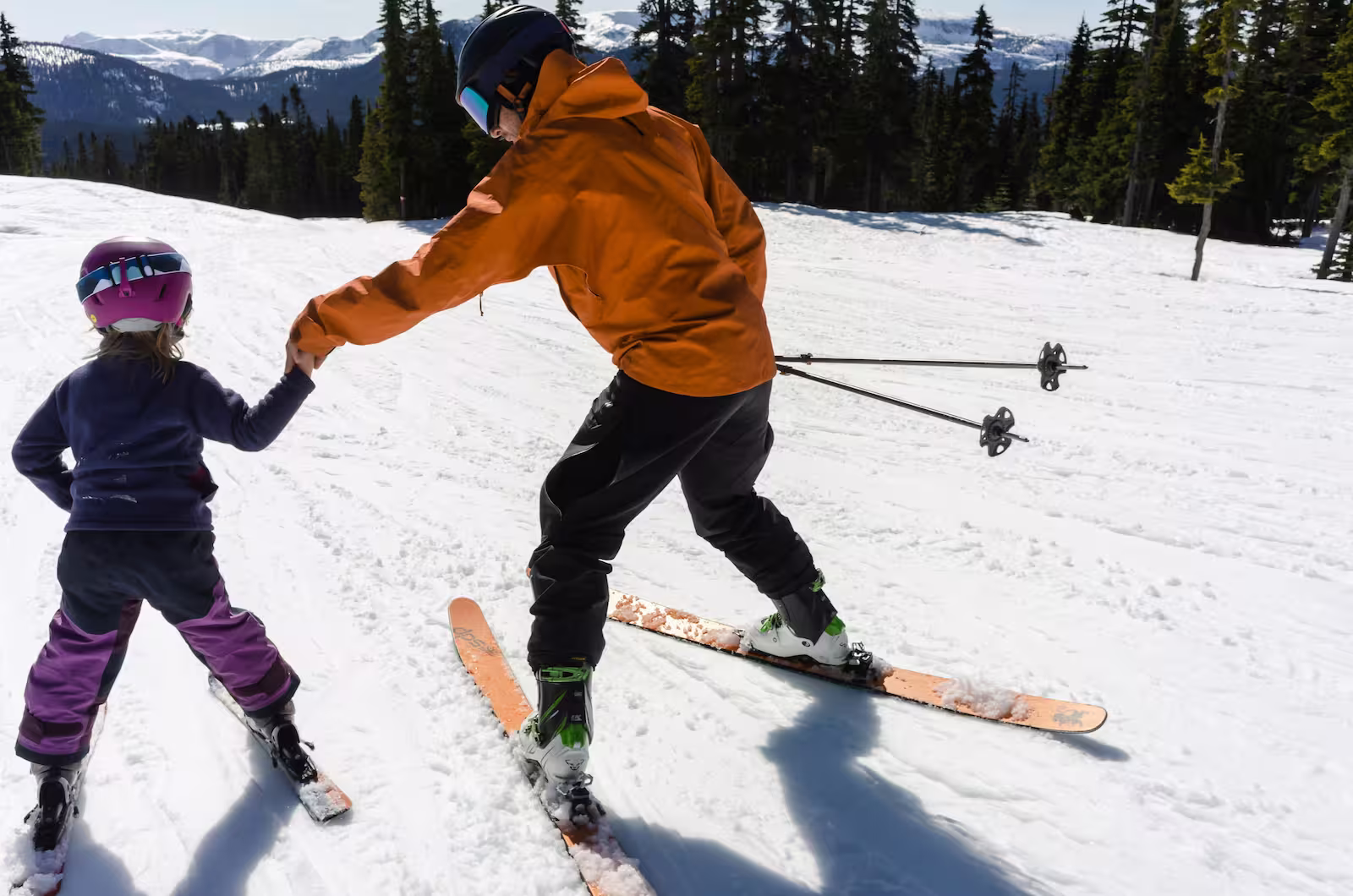 Skiing instructor holds a hand of a practicing kid