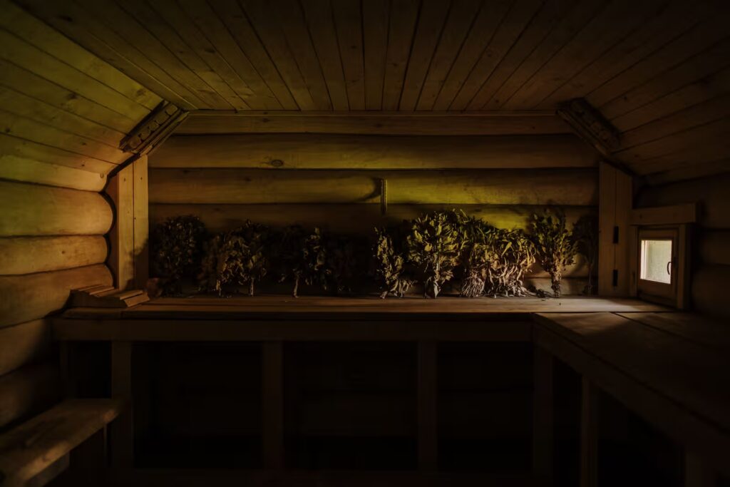 A rustic wooden sauna interior featuring dried plants in warm ambient light, creating a cozy atmosphere.